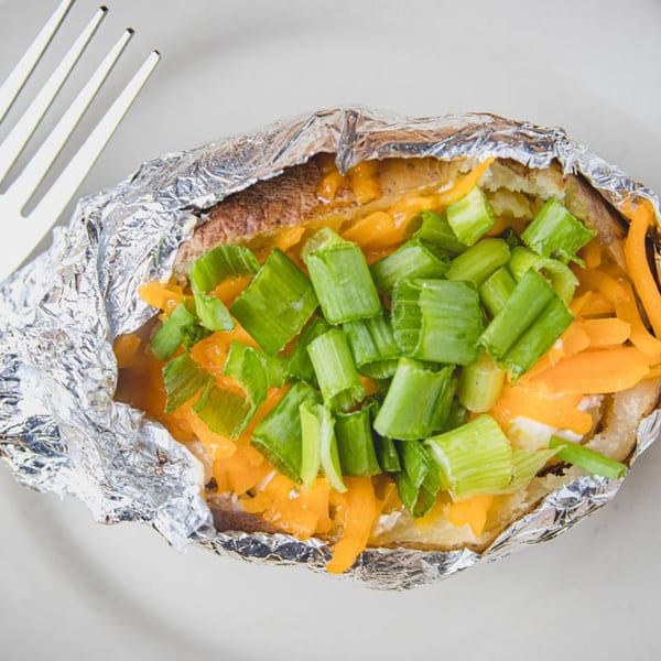 Baked potato with melted cheese, sour cream, and green onions, served in foil with a fork.