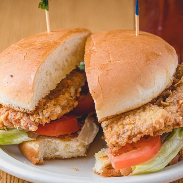 Two halves of a crispy fried chicken sandwich with lettuce and tomato on a white plate.