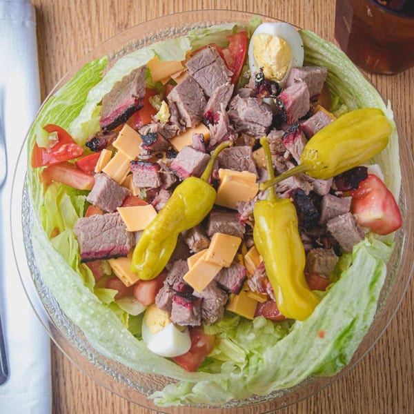 Overhead view of a Barbecue Inn salad with brisket, cheese, tomatoes, hard-boiled egg, and peppers.