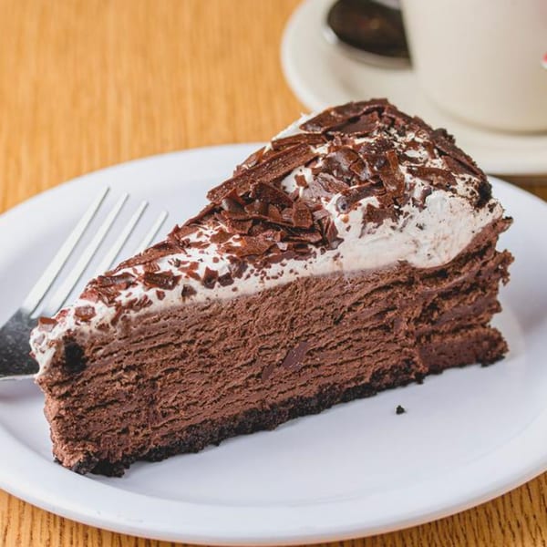 A slice of rich chocolate cheesecake with whipped cream and chocolate shavings on a white plate.