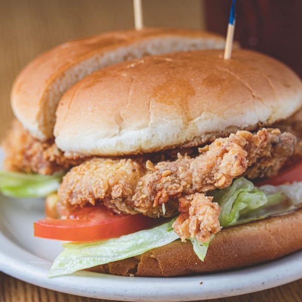 Crispy fried chicken sandwich with lettuce and tomato on a bun, held by a toothpick.