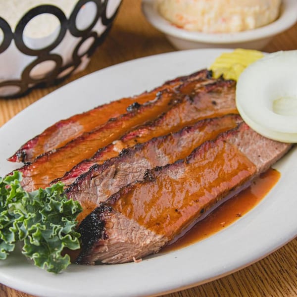 Slices of Barbecue Inn's brisket with sauce, kale, onion, and pickles on a white plate.